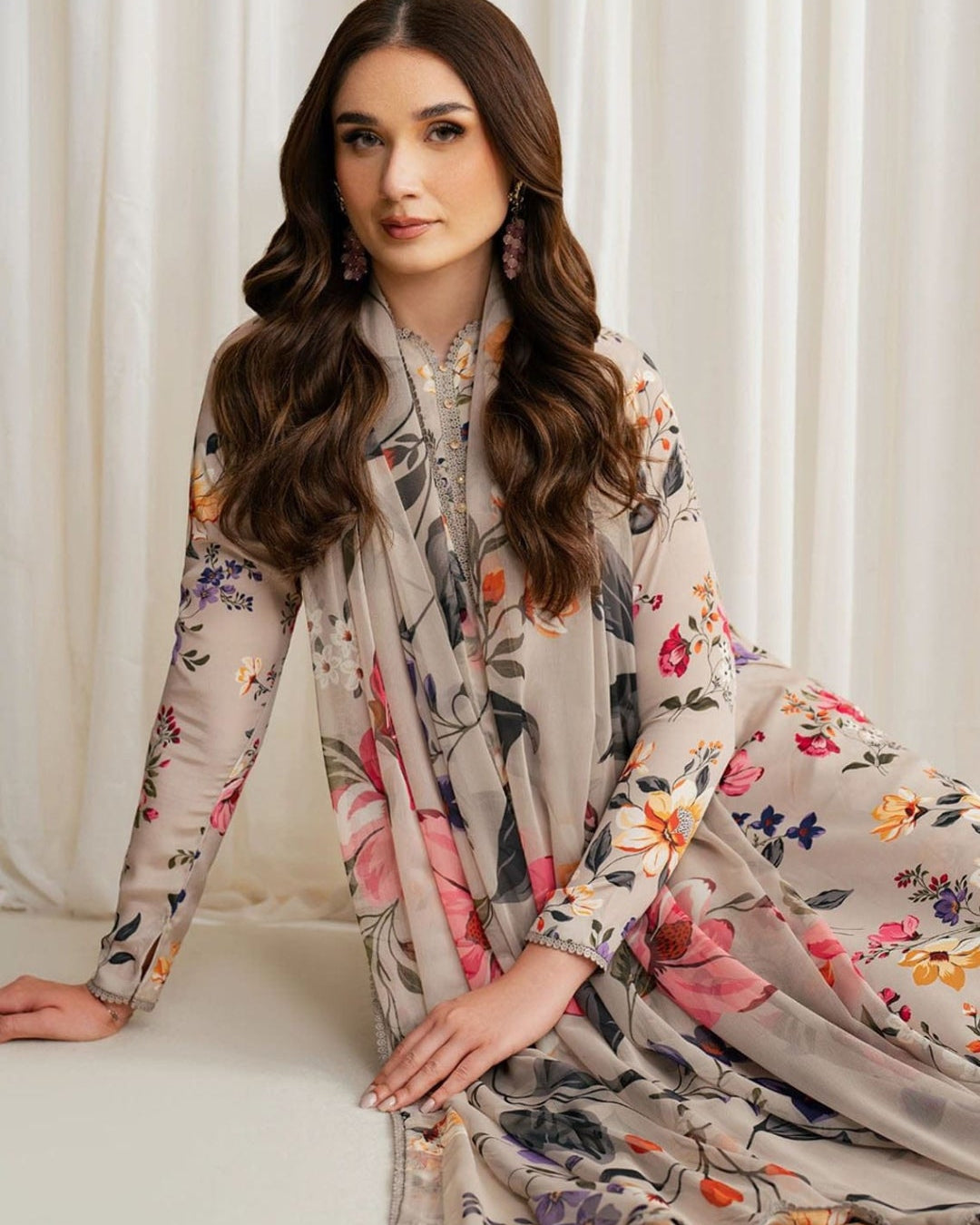 Woman wearing a floral dress sitting against a white curtain