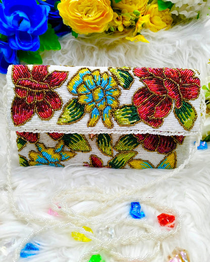 A multicolored floral-patterned clutch purse with a beaded chain, displayed on a white surface with a blue and yellow flower arrangement and colorful beads nearby.