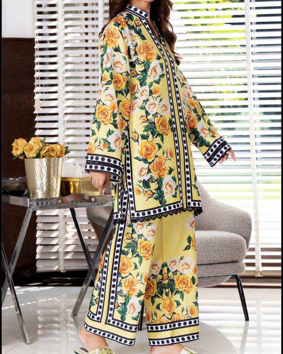 Woman wearing a floral dress standing in a room with a table and flowers.