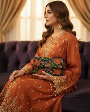 Woman in traditional orange outfit with embroidery, holding a clutch, sitting on a couch.