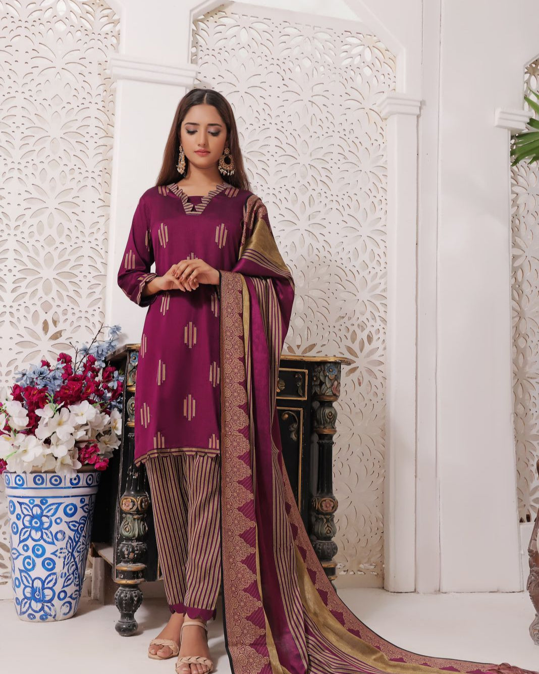 Woman in a purple traditional outfit with a matching dupatta in a decorative setting.